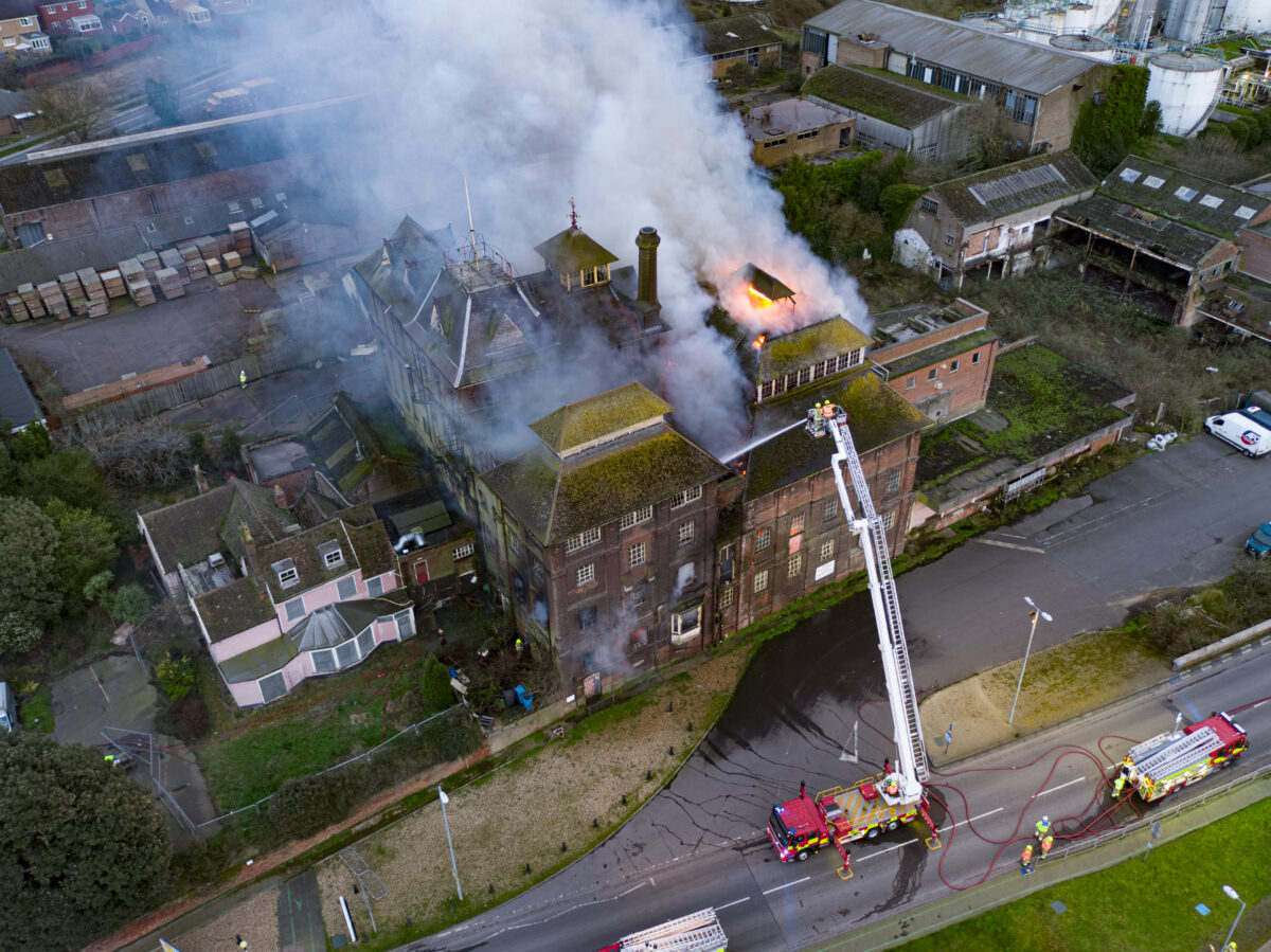A photograph of a Victorian brick building on fire. A fire engine is attempting to put the fire out using an aerial platform.